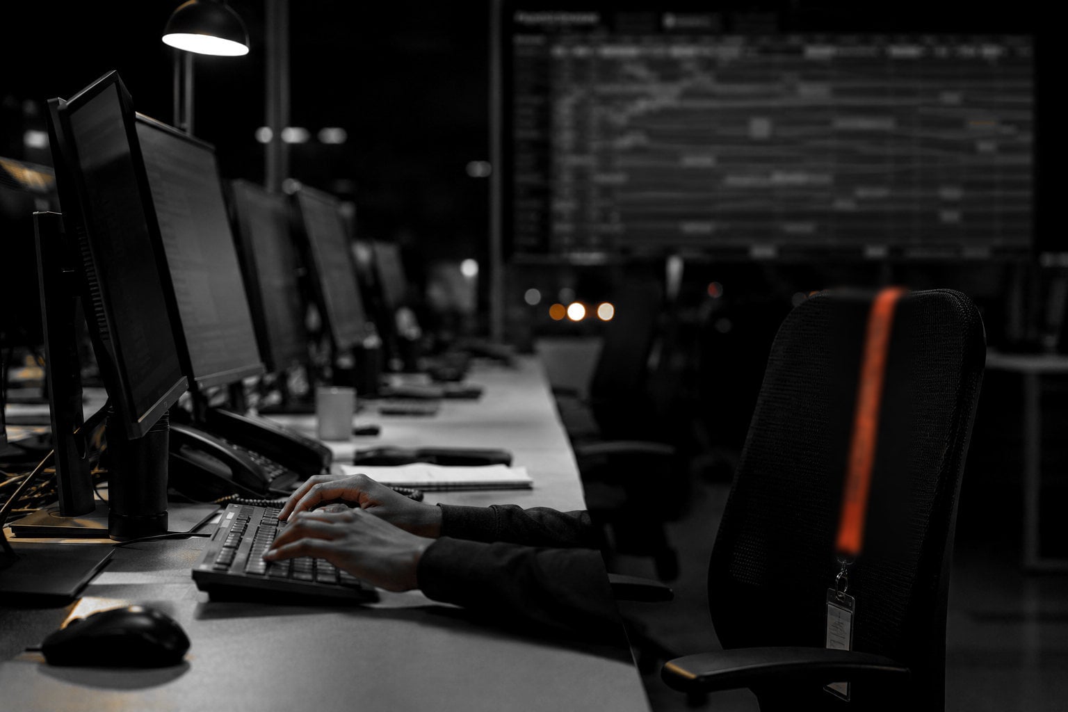 A freight operations room at night, monitors along a shared desk and a lane chart on the far wall.